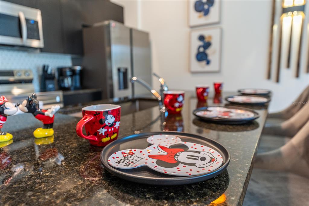 A kitchen island features Minnie Mouse-themed plates and mugs on a dark granite countertop — 3405 TRANQUIL TRAIL, KISSIMMEE, FL