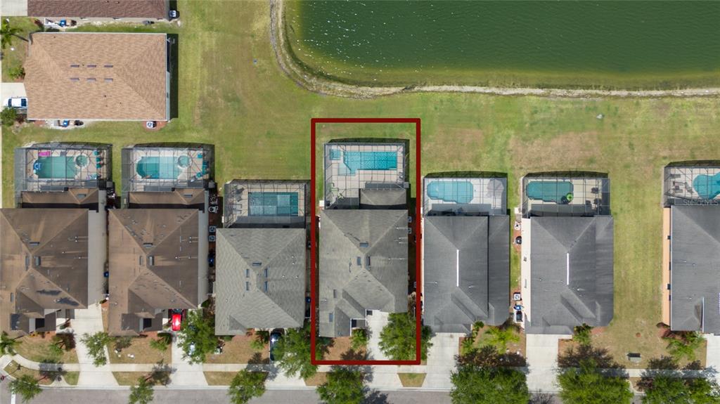 An aerial view shows a suburban neighborhood with houses featuring swimming pools near a lake — 1006 TOURMALINE DRIVE, KISSIMMEE, FL