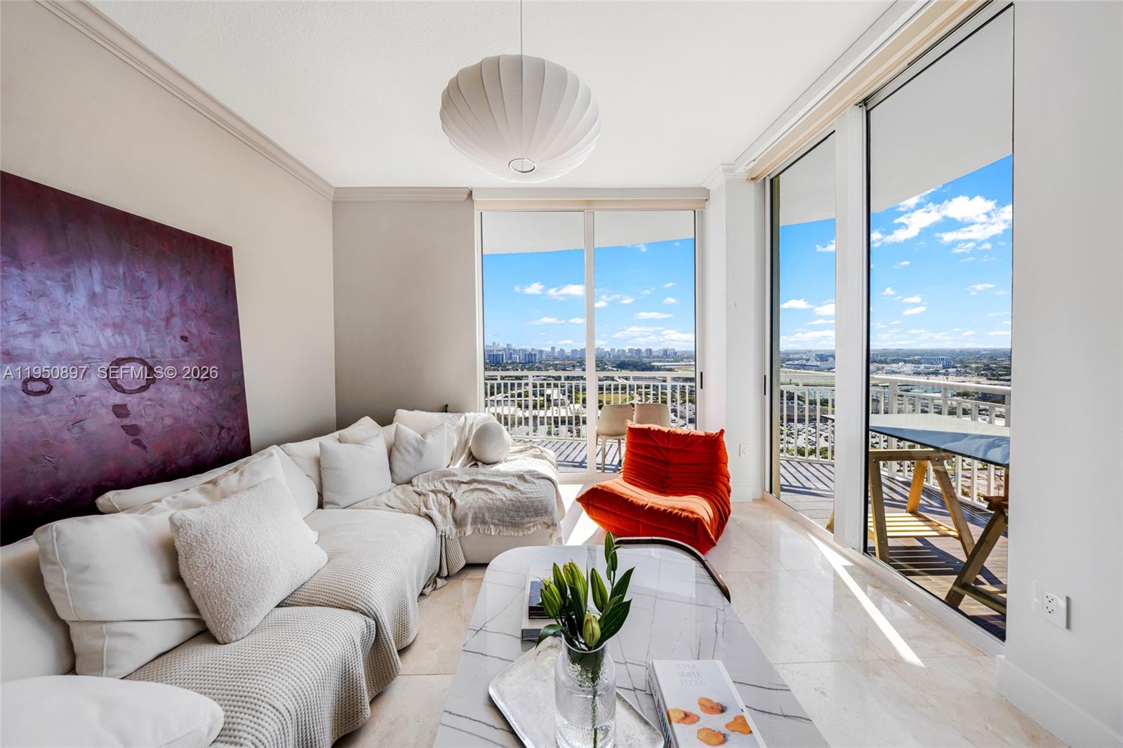 A modern living room features a white sectional sofa, orange chair, and floor-to-ceiling balcony windows — 1745 E Hallandale Beach Blvd # 2407W, Hallandale Beach FL 33009, HALLANDALE BEACH, FL