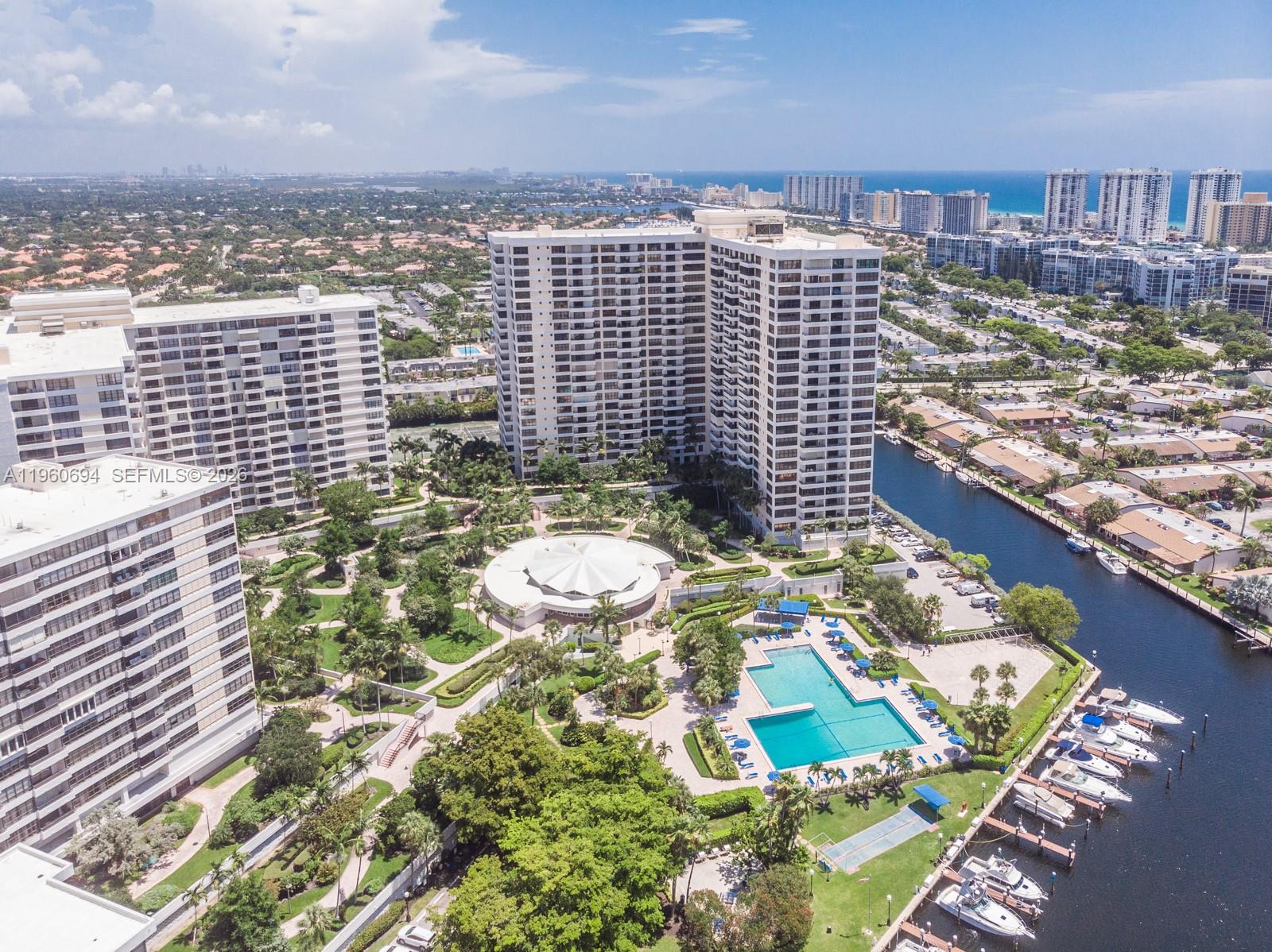 An aerial view shows high-rise apartment buildings, a swimming pool, and a boat-lined canal — 600 Three Islands Blvd # 411, Hallandale Beach FL 33009, HALLANDALE BEACH, FL