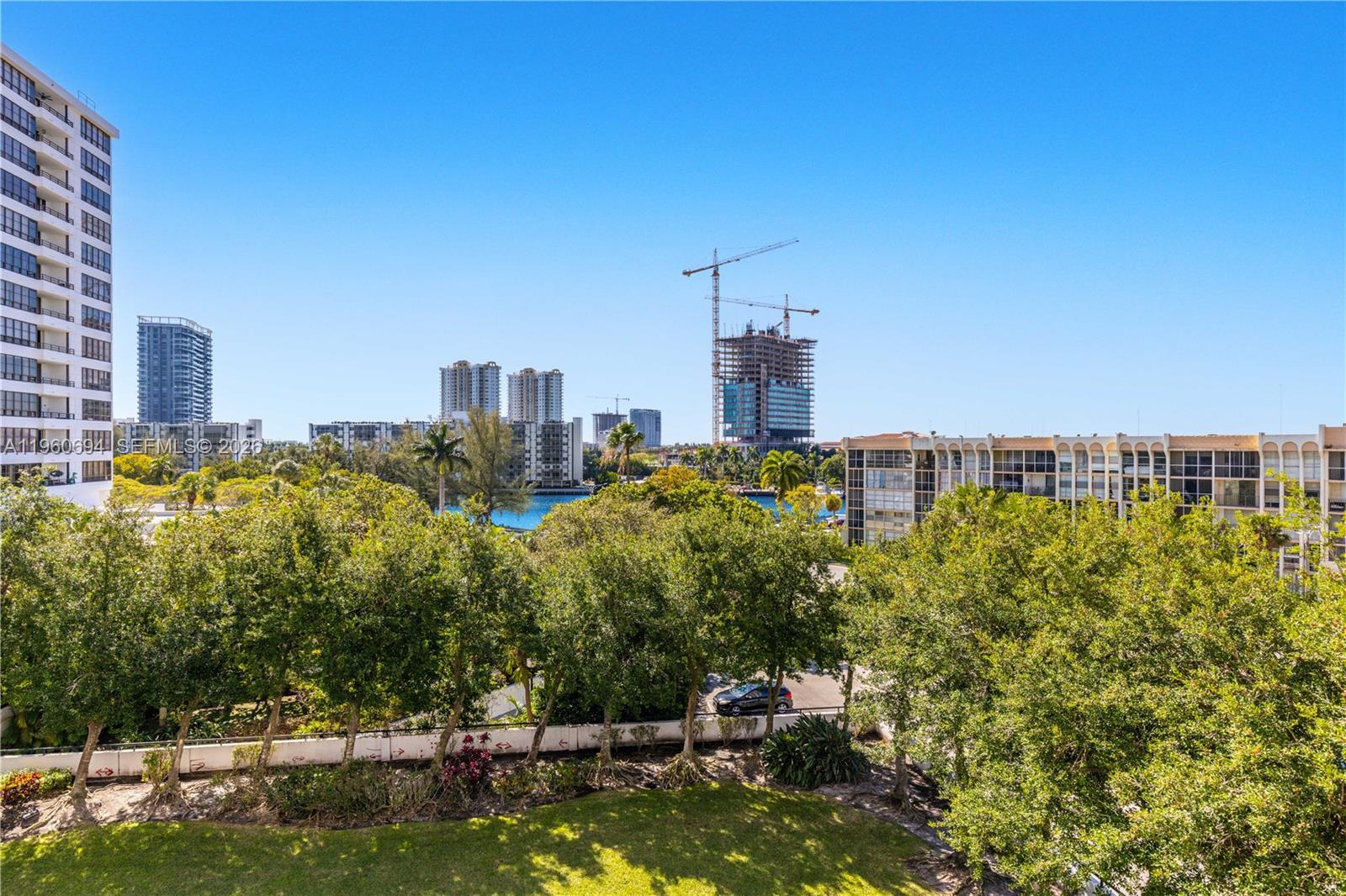 An elevated view of a grassy area, trees, and surrounding apartment buildings under a clear sky — 600 Three Islands Blvd # 411, Hallandale Beach FL 33009, HALLANDALE BEACH, FL