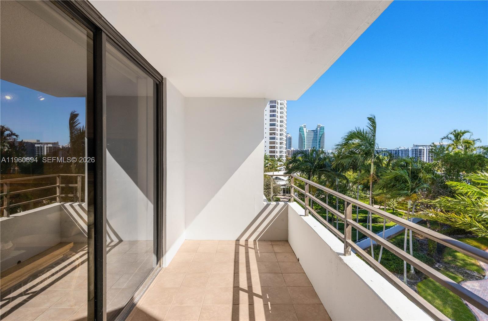 A balcony with tiled flooring, a metal railing, and views of palm trees and buildings — 600 Three Islands Blvd # 411, Hallandale Beach FL 33009, HALLANDALE BEACH, FL