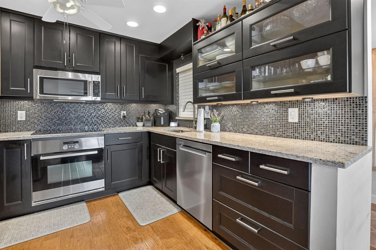 A kitchen features dark cabinets, stainless steel appliances, a mosaic tile backsplash, and granite countertops — 8617 W Boca Glades Boulevard # H, Boca Raton FL 33434, BOCA RATON, FL