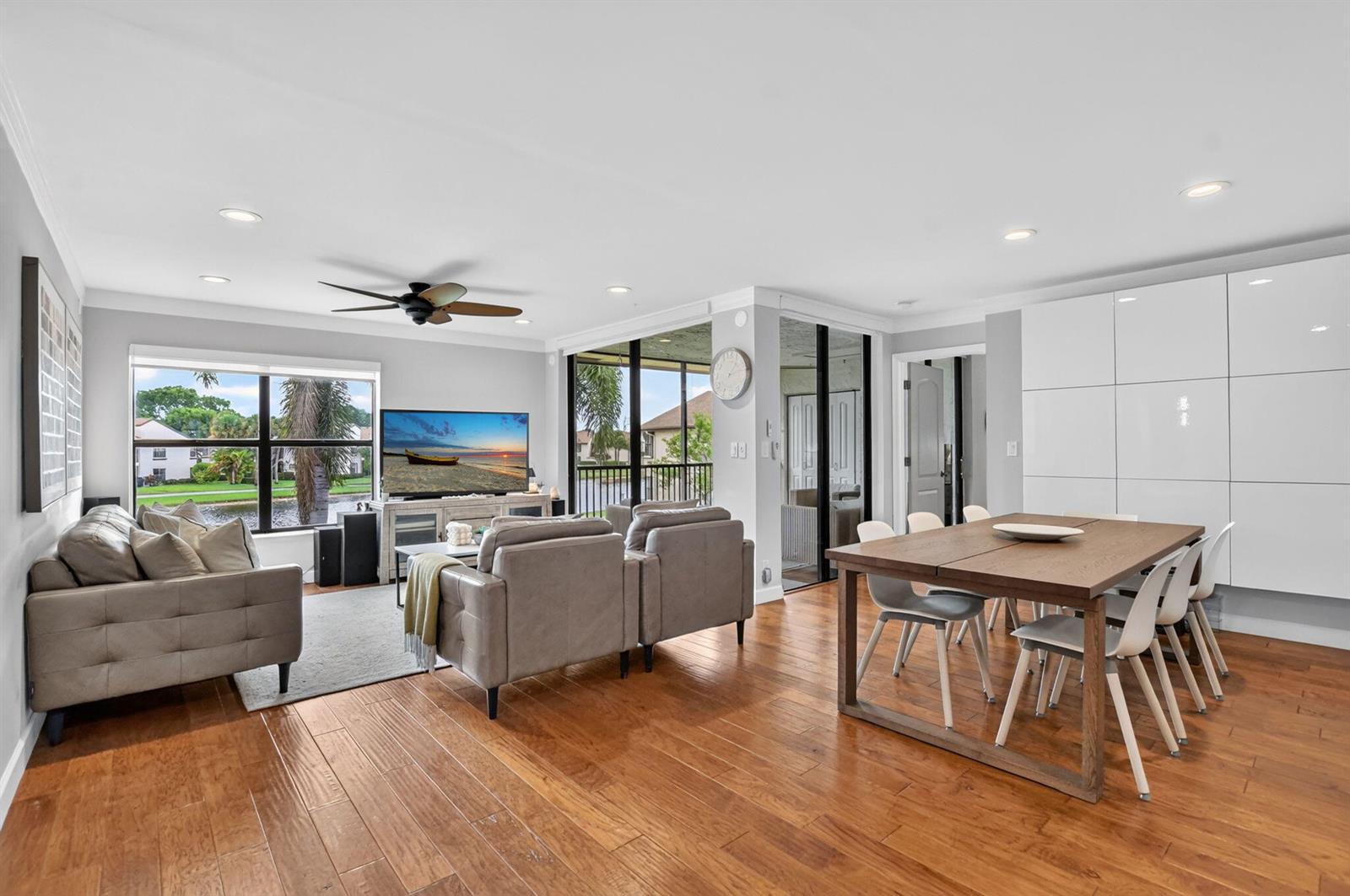 An open-concept living and dining area features hardwood floors, a gray sofa, and white cabinetry — 8617 W Boca Glades Boulevard # H, Boca Raton FL 33434, BOCA RATON, FL