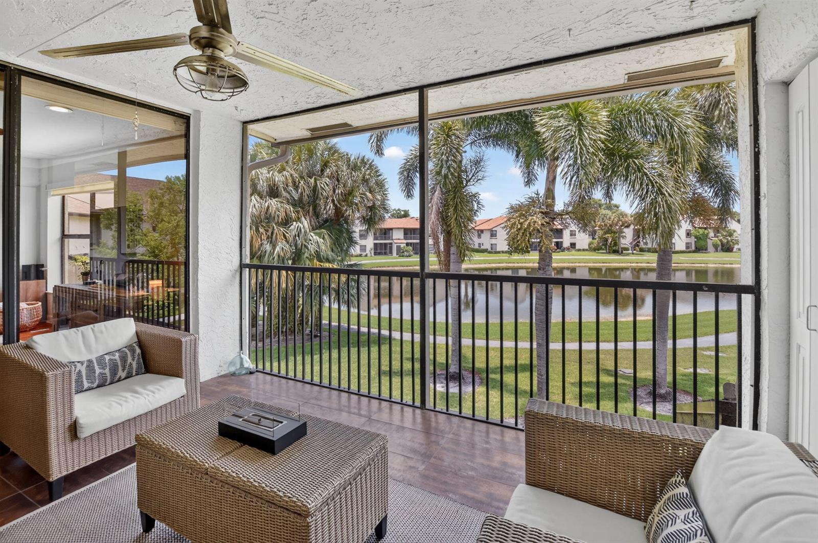 A screened-in balcony with wicker furniture overlooks a pond and palm trees — 8617 W Boca Glades Boulevard # H, Boca Raton FL 33434, BOCA RATON, FL
