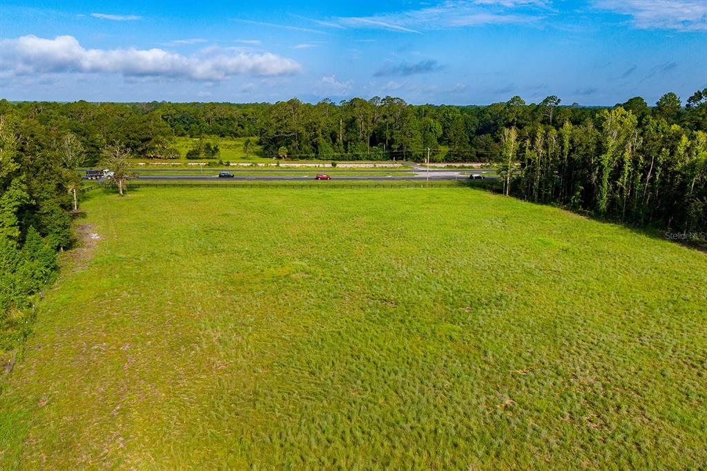 An aerial view shows a large, grassy, undeveloped field bordered by trees and a highway — TBD 000 SE HWY 301, HAWTHORNE, FL
