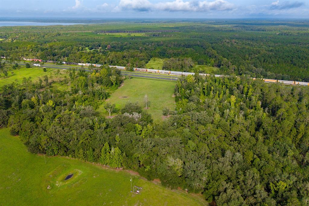 An aerial view shows a large, grassy field bordered by dense forest and a railroad track — TBD 000 SE HWY 301, HAWTHORNE, FL