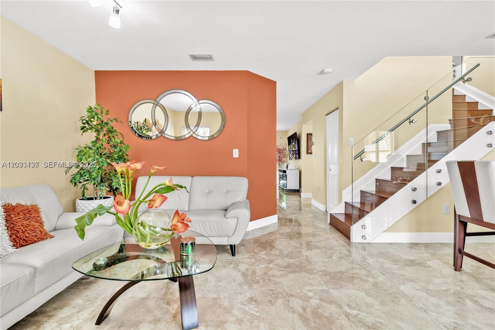 A living room features a terracotta accent wall, glass-topped table, and a modern glass-railed staircase — 16453 SW 97th St # 0, Miami FL 33196, MIAMI, FL