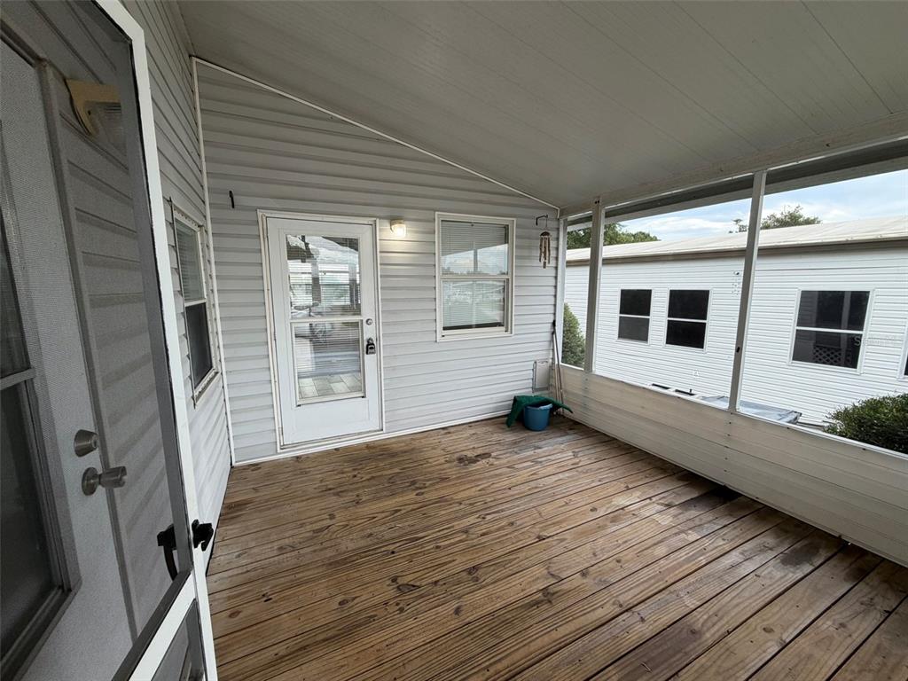 A covered wooden porch features light gray siding, a screen enclosure, and a white door — 50989 HIGHWAY 27 UNIT 33, DAVENPORT, FL