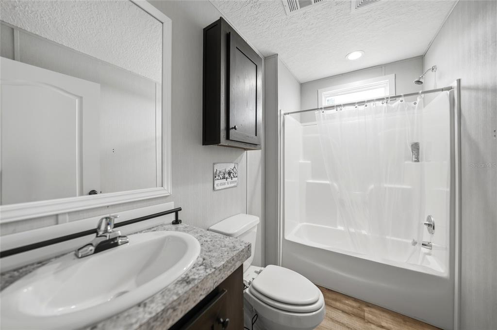 A bathroom features a vanity with a granite countertop, a toilet, and a shower-tub combo — 11587 SE FOSTER AVENUE, ARCADIA, FL
