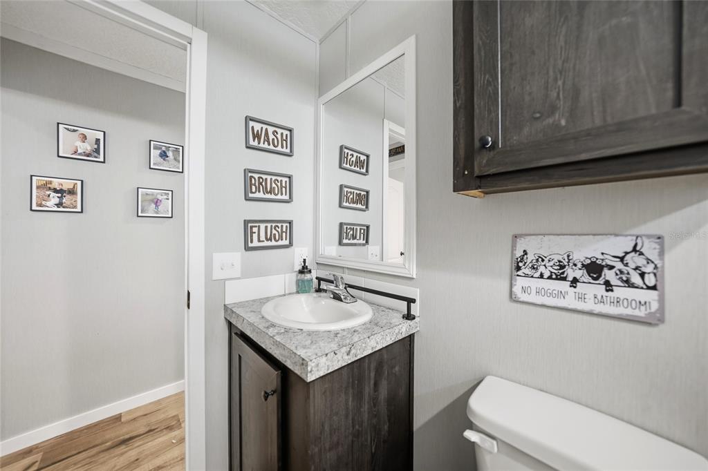 A bathroom features a dark wood vanity, a stone-look countertop, and wall-mounted decorative signs — 11587 SE FOSTER AVENUE, ARCADIA, FL