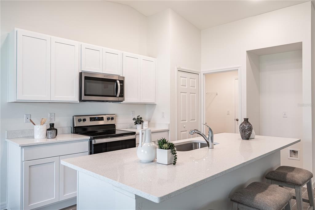 A modern kitchen features white cabinets, stainless steel appliances, and a large quartz-topped island — 5202 BRUNSWICK TERRACE, PORT CHARLOTTE, FL