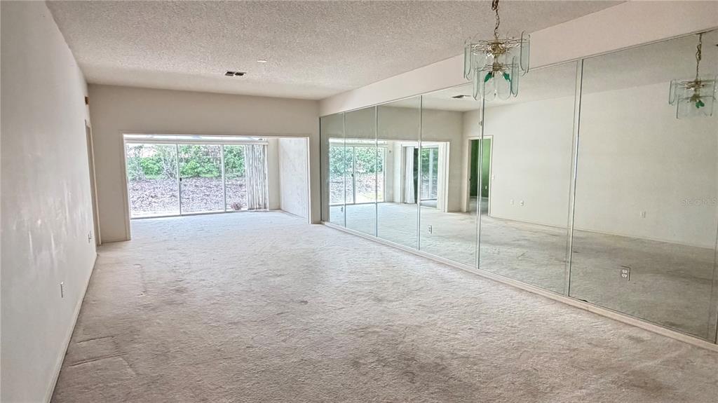 A living room features beige carpeting, a mirrored wall, and sliding glass doors to outside — 1 ENCLAVE DRIVE, WINTER HAVEN, FL