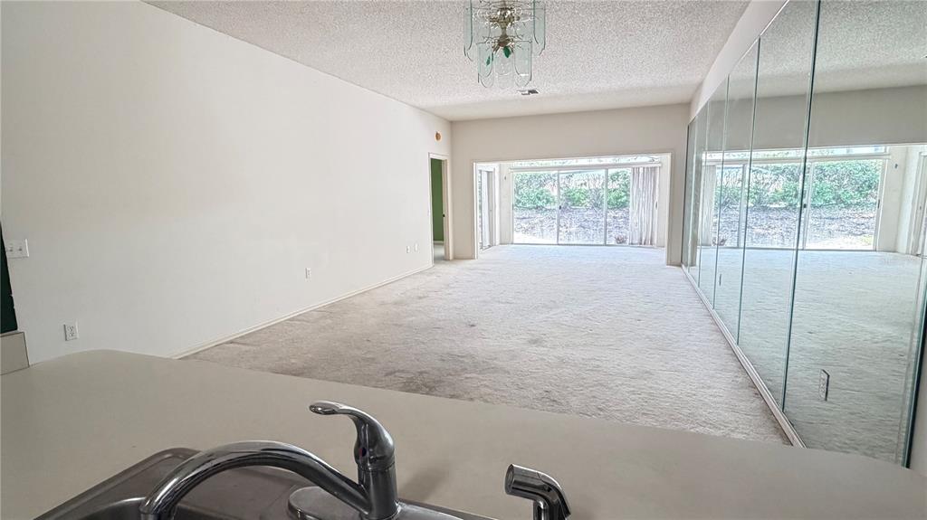 A kitchen sink overlooks a carpeted living room with a mirrored wall and sliding glass doors — 1 ENCLAVE DRIVE, WINTER HAVEN, FL