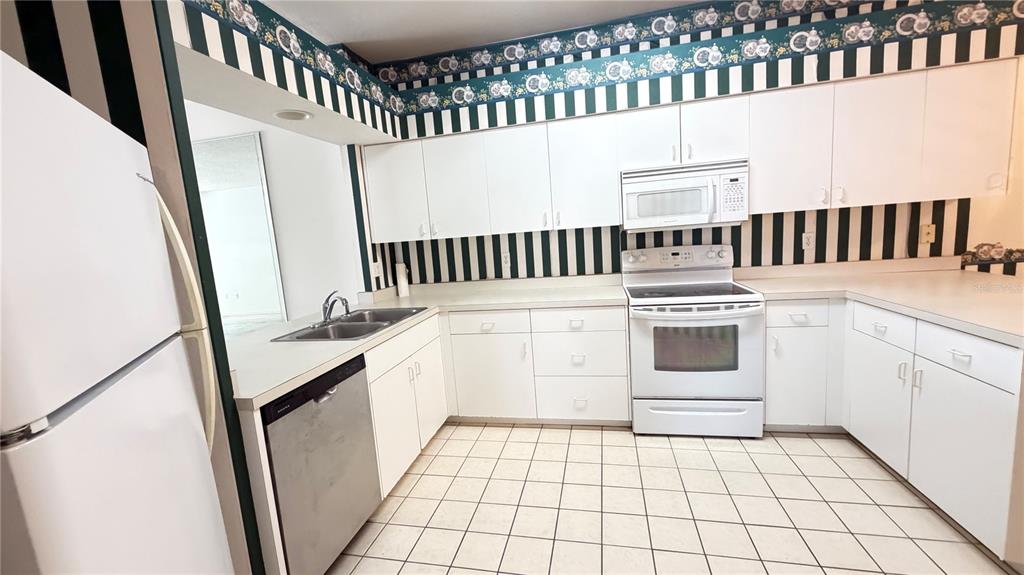 A kitchen features white cabinets, white appliances, a tiled floor, and black-and-white striped wallpaper — 1 ENCLAVE DRIVE, WINTER HAVEN, FL