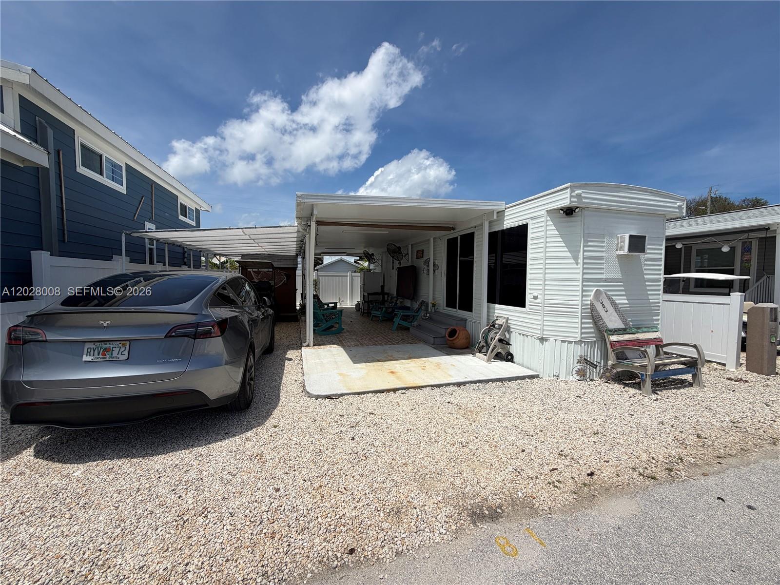 A gray car is parked on a gravel lot next to a white mobile home — 325 Calusa Street, Key Largo FL 33037, KEY LARGO, FL