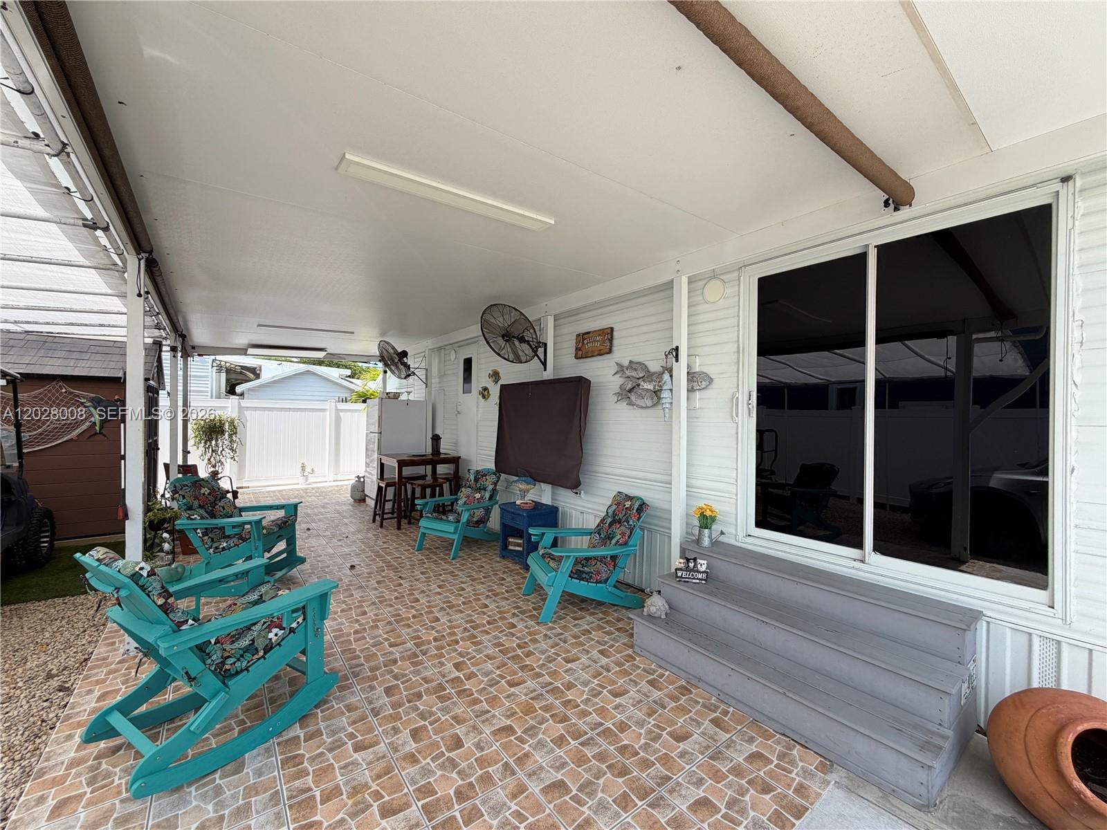 A covered patio features tiled flooring, several turquoise rocking chairs, and steps leading to a sliding door — 325 Calusa Street, Key Largo FL 33037, KEY LARGO, FL