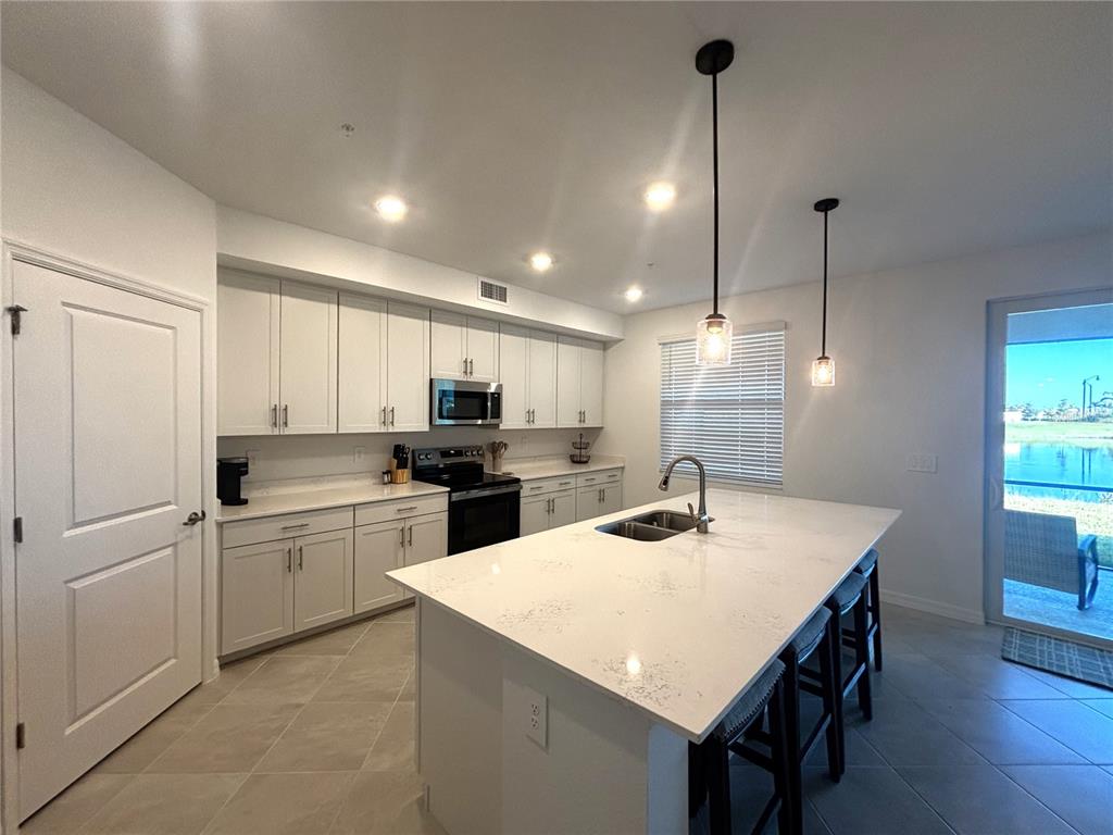 A kitchen features white cabinets, a quartz-topped island with a sink, and tile flooring — 17745 BORACAY COURT UNIT 101, VENICE, FL