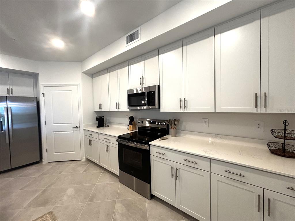 A kitchen features white cabinetry, stainless steel appliances, and light-colored countertops — 17745 BORACAY COURT UNIT 101, VENICE, FL