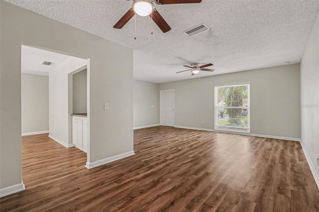 An empty living room features wood-look flooring, two ceiling fans, and a white door — 3607 WOODHILL DRIVE, BRANDON, FL