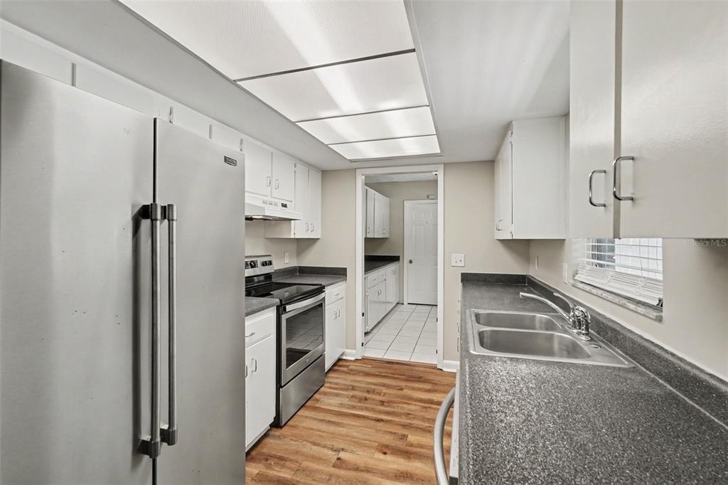 A kitchen features white cabinets, stainless steel appliances, dark countertops, and wood-look flooring — 3607 WOODHILL DRIVE, BRANDON, FL