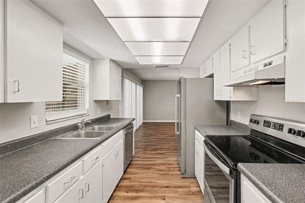 A galley kitchen features white cabinets, gray countertops, stainless steel appliances, and wood-look flooring — 3607 WOODHILL DRIVE, BRANDON, FL