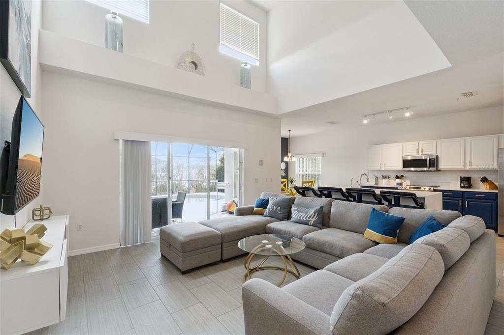 A living room with high ceilings, gray sectional sofa, and an open kitchen with island — 652 HIGHGATE PARK BOULEVARD, DAVENPORT, FL