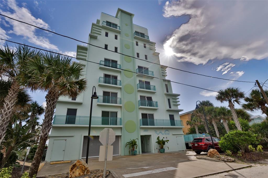 A light green multi-story apartment building with balconies and palm trees under a sunny sky — 2801 HILL STREET UNIT 502, NEW SMYRNA BEACH, FL