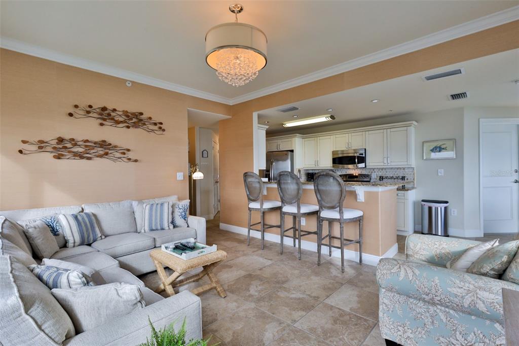 A living room with a sectional sofa, kitchen bar seating, and neutral tile flooring — 2801 HILL STREET UNIT 502, NEW SMYRNA BEACH, FL