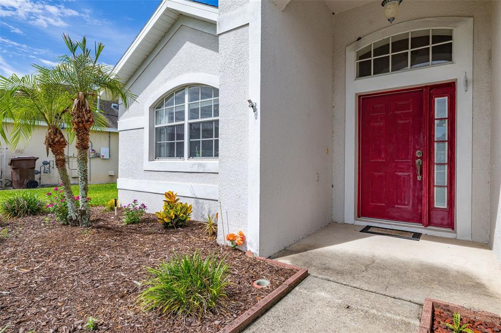 A red front door with a sidelight and transom window sits beside a landscaped yard — 135 JESSAMINE DRIVE, DAVENPORT, FL