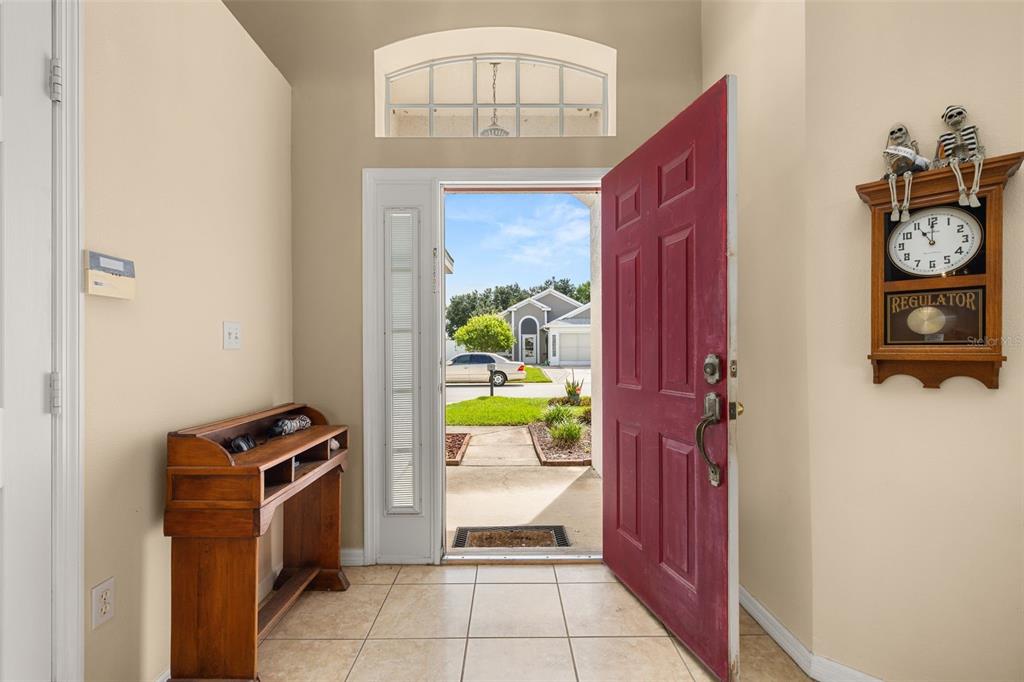 An entryway features a red door, tile flooring, a wooden console table, and a wall clock — 135 JESSAMINE DRIVE, DAVENPORT, FL