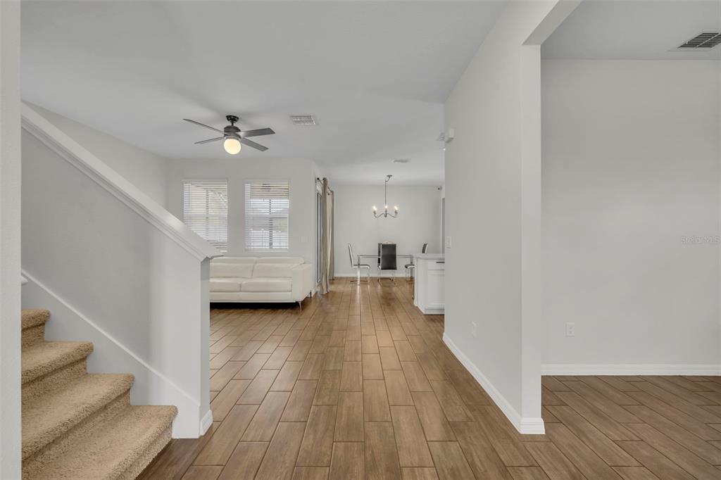 A view from the bottom of a carpeted staircase looking toward a living and dining area — 11844 FOUNDERS STREET, ORLANDO, FL
