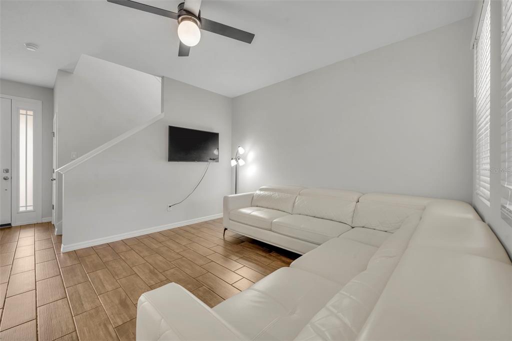 A living room features a white sectional sofa, wall-mounted television, and wood-look tile flooring — 11844 FOUNDERS STREET, ORLANDO, FL