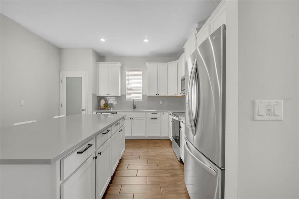 A modern kitchen features white cabinetry, stainless steel appliances, a large island, and wood-look flooring — 11844 FOUNDERS STREET, ORLANDO, FL