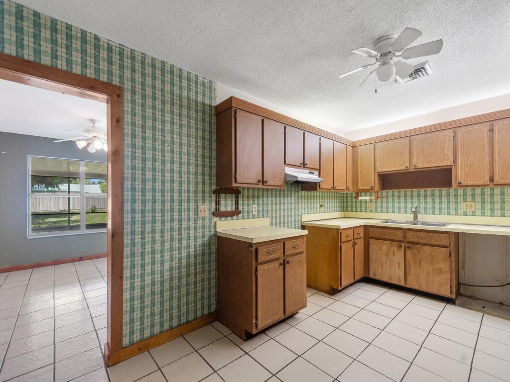 A kitchen with wood cabinets, yellow countertops, plaid wallpaper, and white tiled floors — 2309 NE 13th Court, Jensen Beach FL 34957, JENSEN BEACH, FL