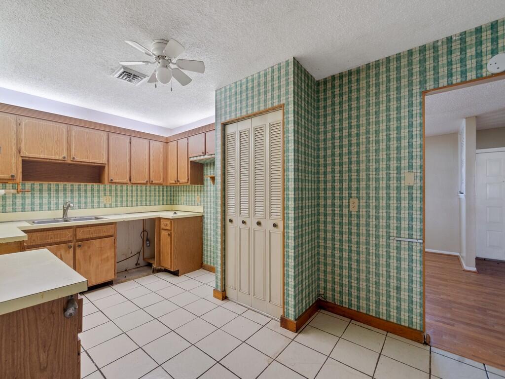 A kitchen with wood cabinets, green plaid wallpaper, white tile floors, and a ceiling fan — 2309 NE 13th Court, Jensen Beach FL 34957, JENSEN BEACH, FL
