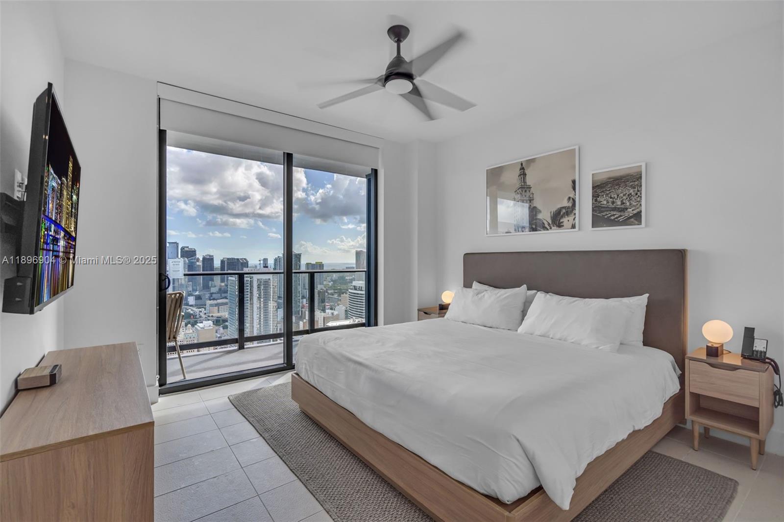 A modern bedroom features a king bed, ceiling fan, and floor-to-ceiling windows overlooking a city — 159 NE 6th St # 4514, Miami FL 33132, MIAMI, FL