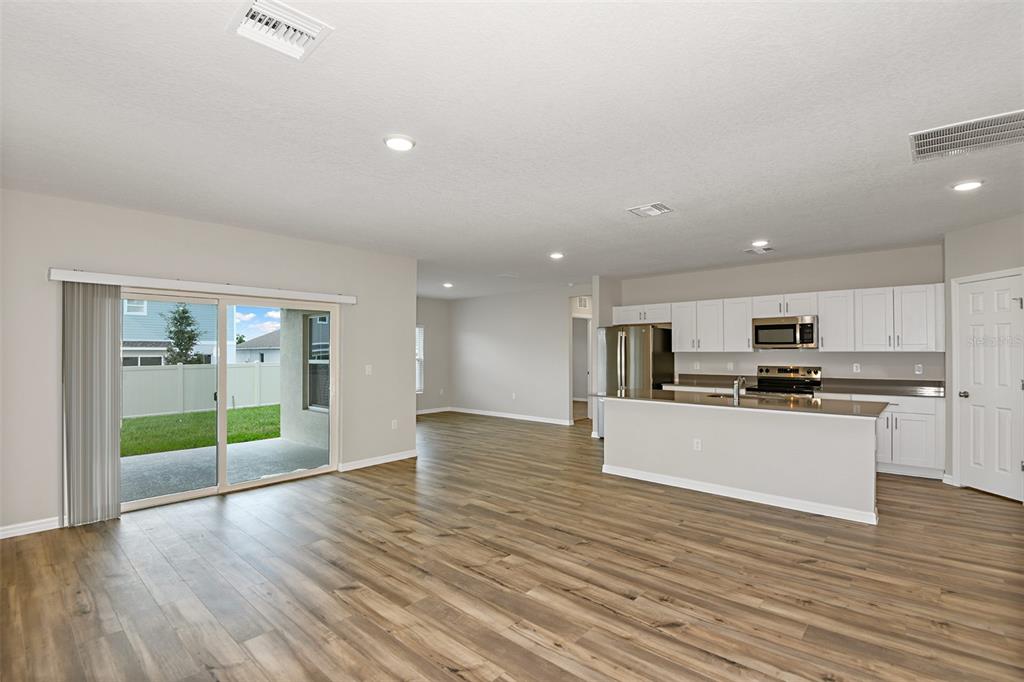 An open-concept kitchen and living area with white cabinets, stainless appliances, and wood-look flooring — 3911 ALTITUDE RUN, DAVENPORT, FL
