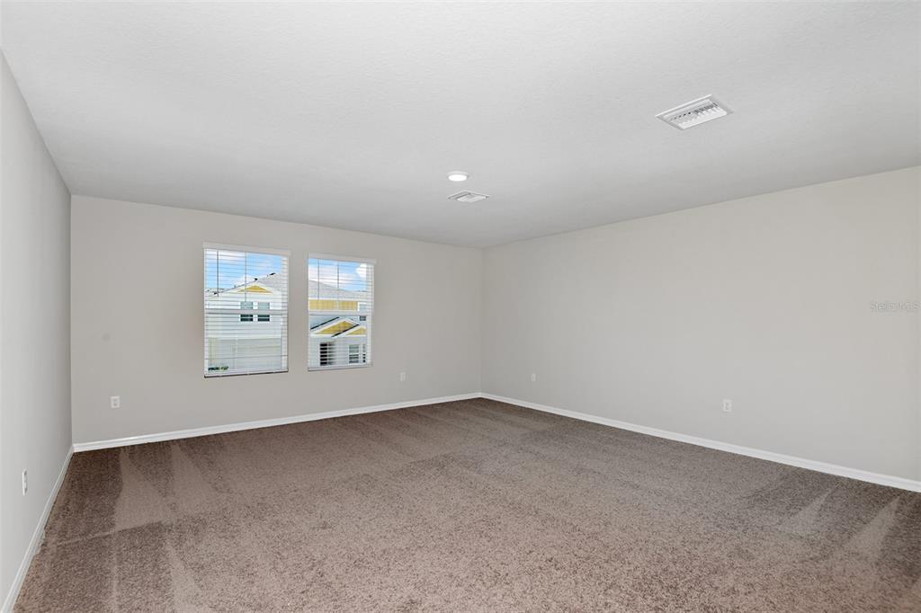 An empty room with beige walls, brown carpeting, and two windows overlooking a neighboring house — 3911 ALTITUDE RUN, DAVENPORT, FL