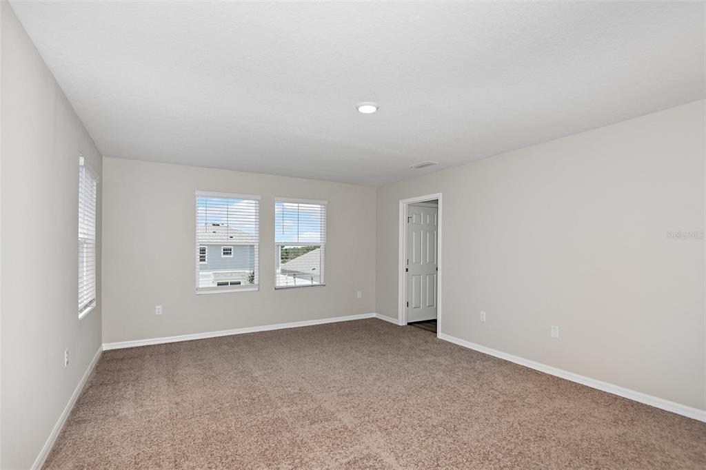 An empty bedroom features beige carpet, light gray walls, two windows, and a doorway — 3911 ALTITUDE RUN, DAVENPORT, FL