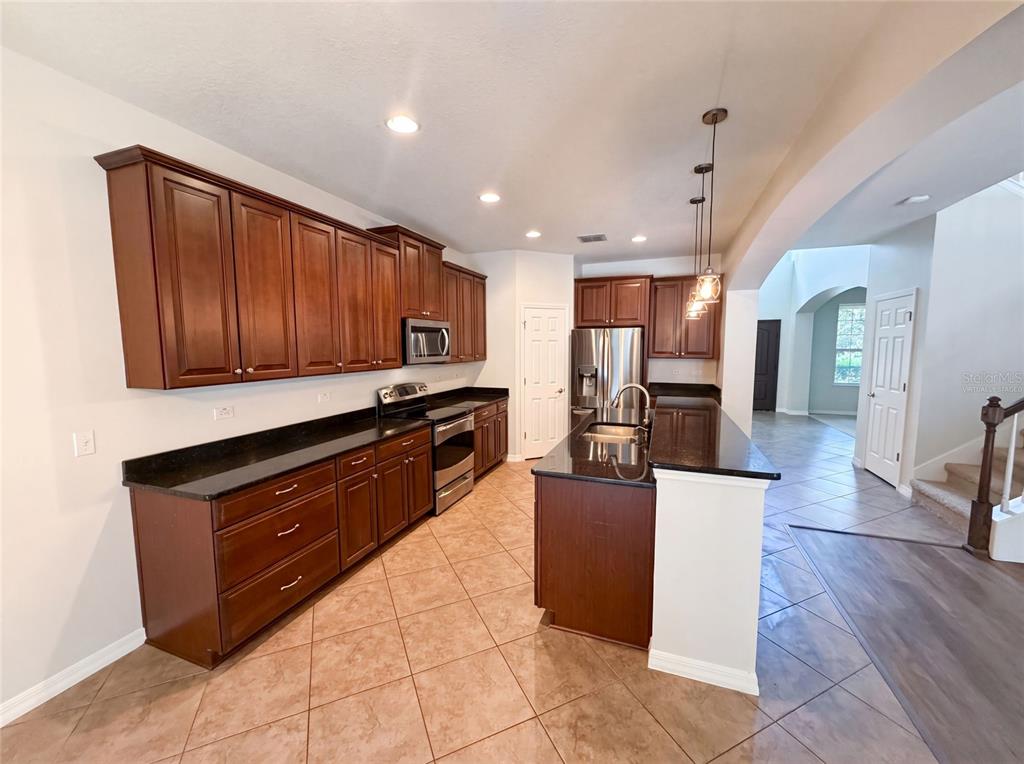 A kitchen with dark wood cabinets, black countertops, stainless steel appliances, and tile flooring — 280 CHANDLER CIRCLE, OVIEDO, FL