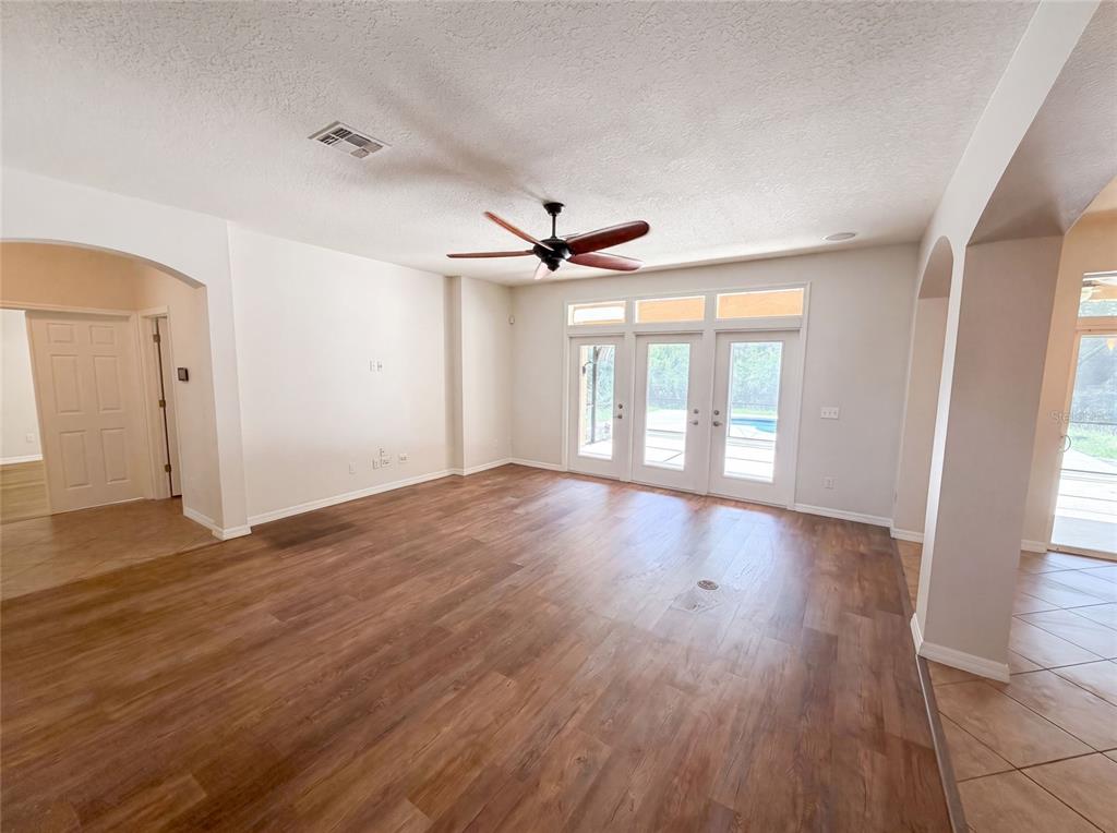 An empty living room features wood-look flooring, a ceiling fan, and glass doors to a pool — 280 CHANDLER CIRCLE, OVIEDO, FL