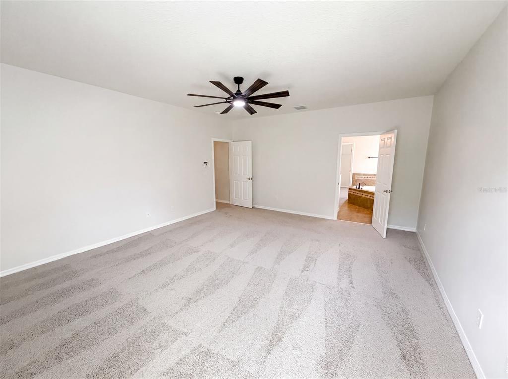 A spacious bedroom features light gray carpet, a ceiling fan, and two open doorways — 280 CHANDLER CIRCLE, OVIEDO, FL