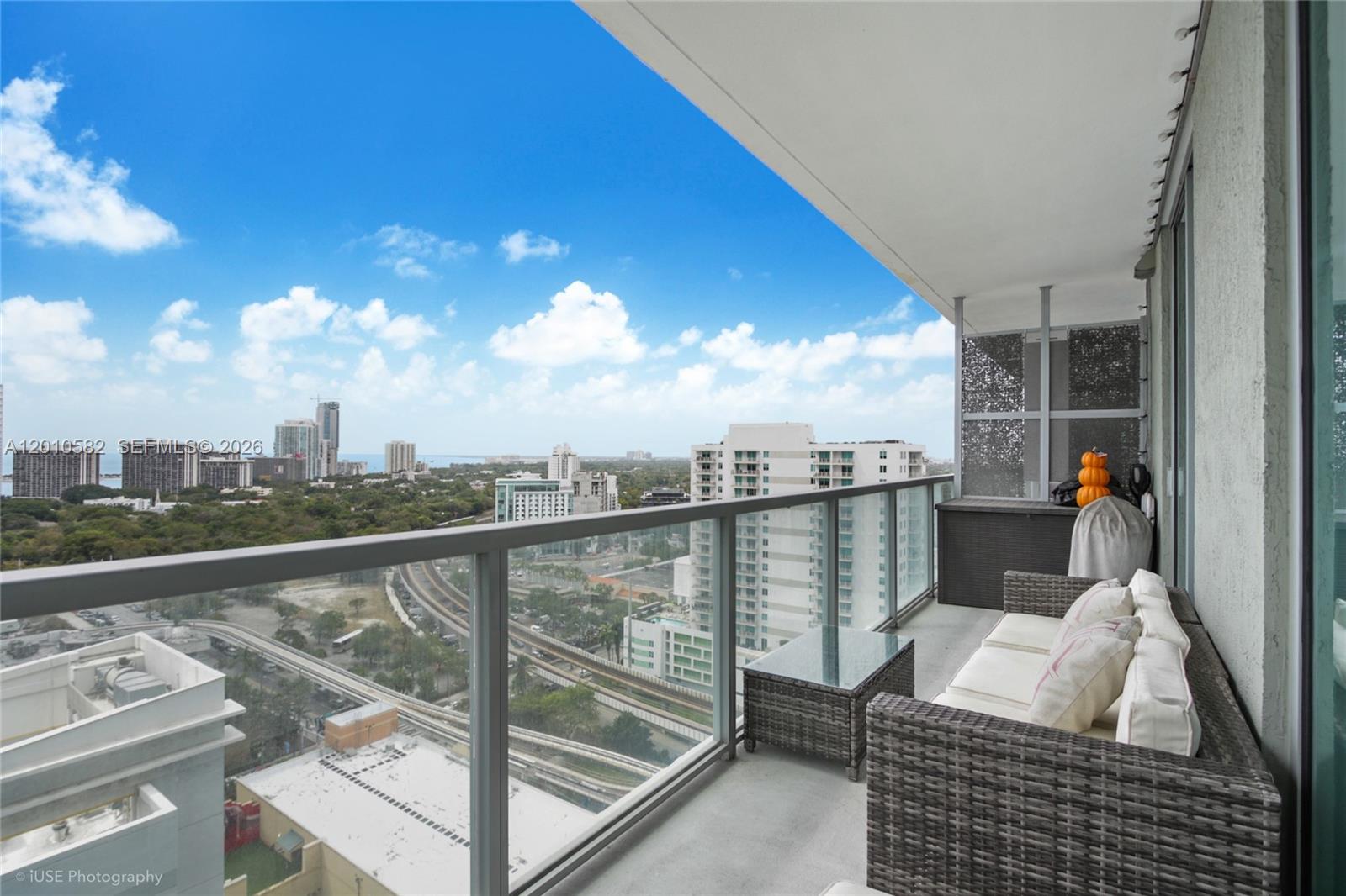 A balcony with wicker furniture overlooks a city skyline and a railway track — 79 SW 12th St, Miami FL 33130, MIAMI, FL