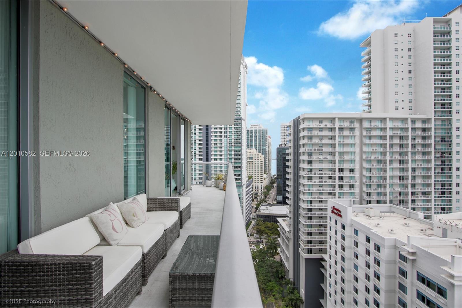 A high-rise balcony features wicker furniture and views of surrounding urban apartment buildings — 79 SW 12th St, Miami FL 33130, MIAMI, FL