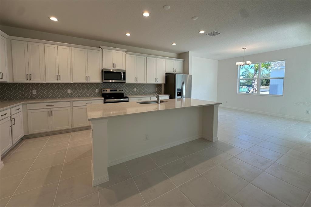 A kitchen with white cabinets, a central island, and tile flooring opens to a dining area — 733 FARFIELDS WAY, DELAND, FL