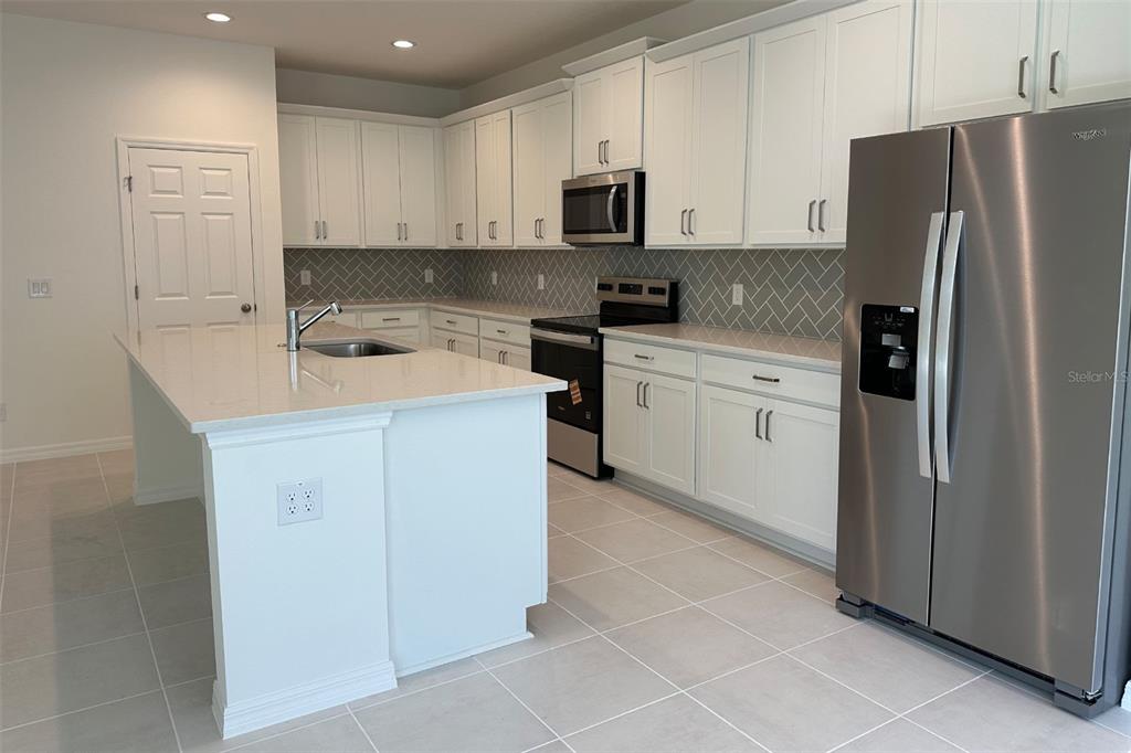 A modern kitchen features white cabinetry, a central island, stainless steel appliances, and herringbone backsplash — 733 FARFIELDS WAY, DELAND, FL