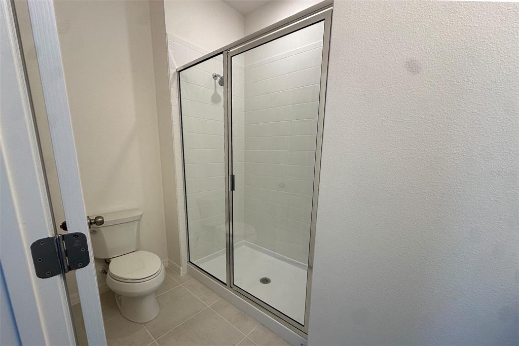 A bathroom features a white toilet and a walk-in shower with glass doors and tile — 733 FARFIELDS WAY, DELAND, FL