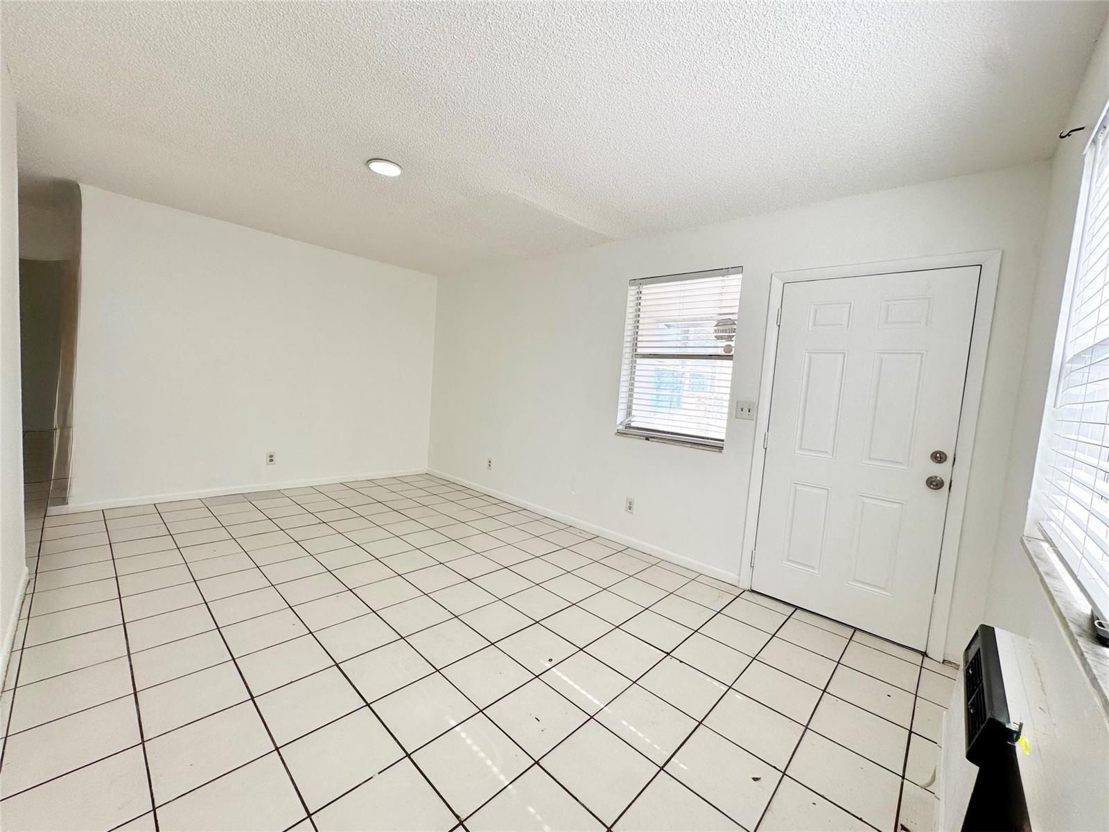An empty room with white walls, white tiled flooring, a window, and a white door — 147 W 17th Street, Riviera Beach FL 33404, RIVIERA BEACH, FL