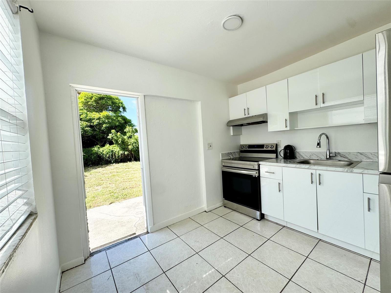 A small kitchen features white cabinets, stainless steel appliances, and a door to the yard — 147 W 17th Street, Riviera Beach FL 33404, RIVIERA BEACH, FL